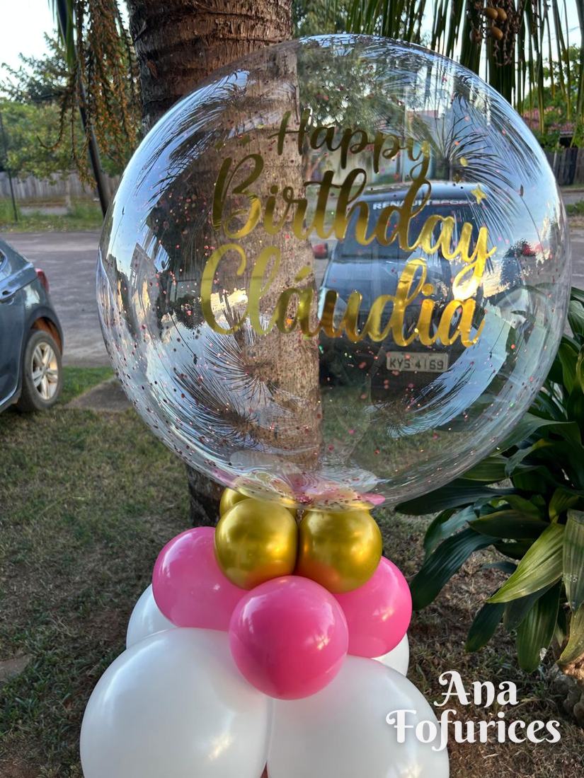 Balão bubble transparente escrito Happy Birthday Cláudia em dourado, com base rosa, dourada e branca