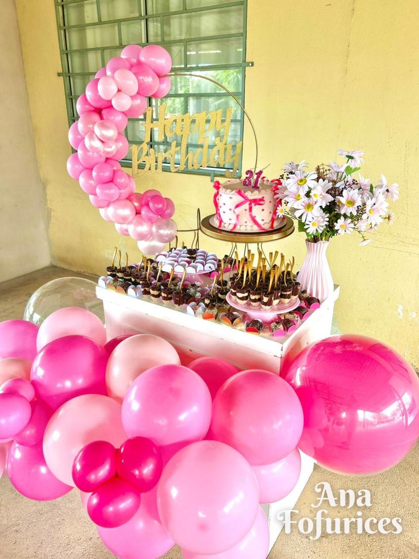 Mesa de aniversário com arco de balões rosa, Happy Birthday dourado, bolo e flores